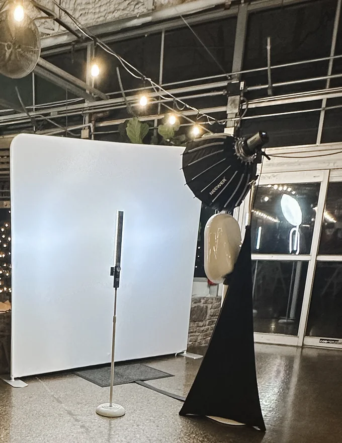 Photo booth setup with a white backdrop and a softbox light on a draped stand under string lights